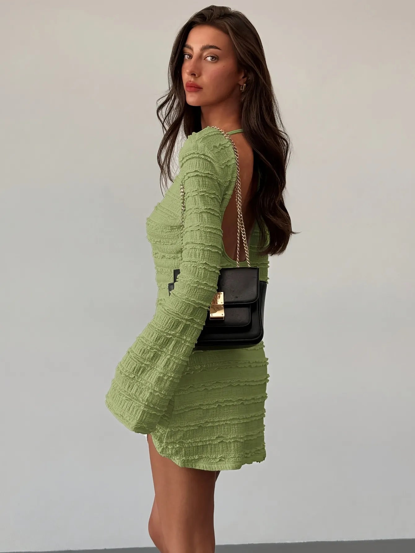 Woman wearing a green textured dress with a black handbag against a plain background