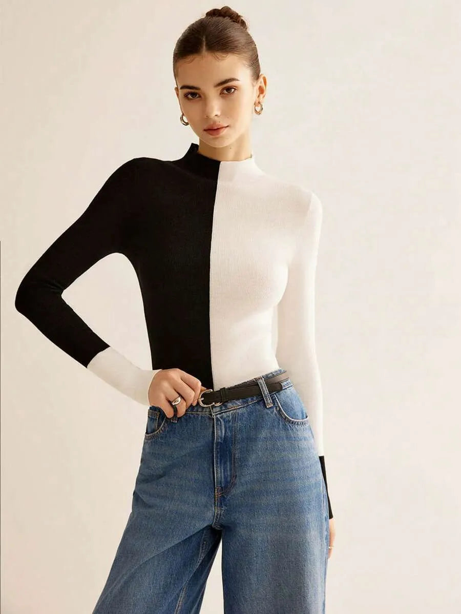 Woman wearing a black and white long-sleeve top with blue jeans on a plain background