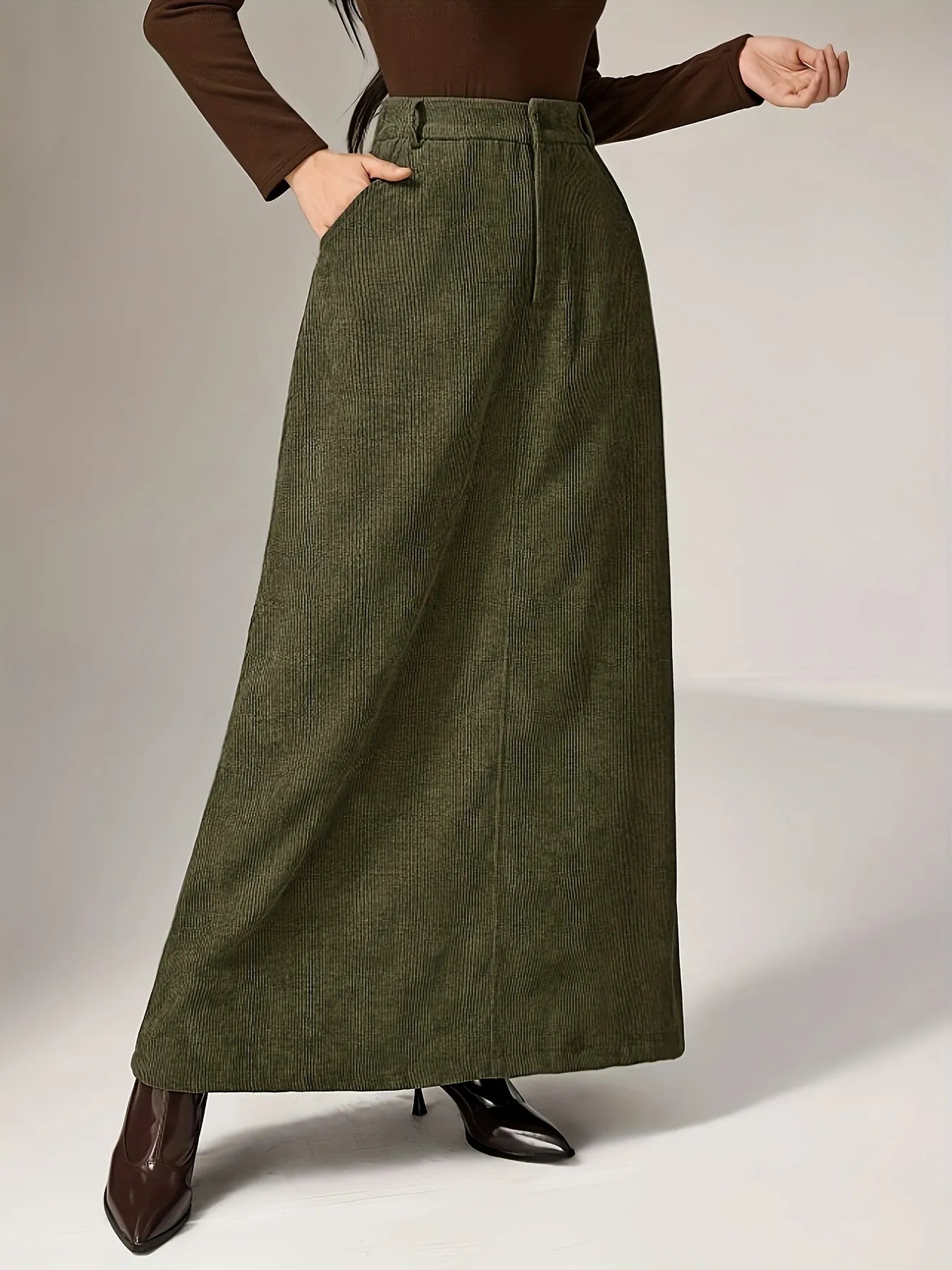 Person wearing a long green skirt with a plain background
