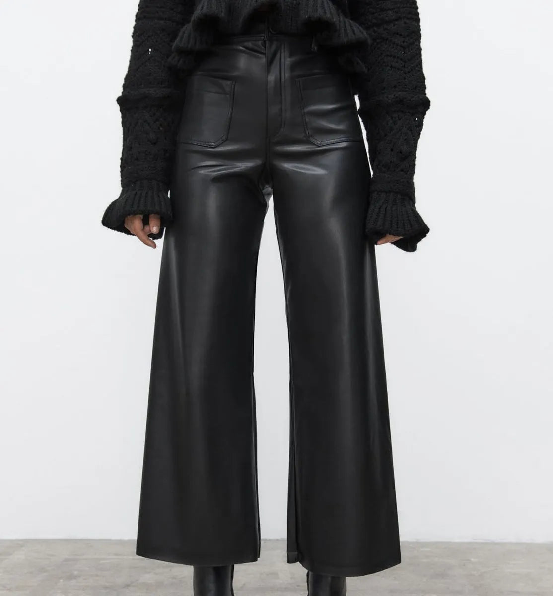 Person wearing black leather wide-leg pants with a plain background