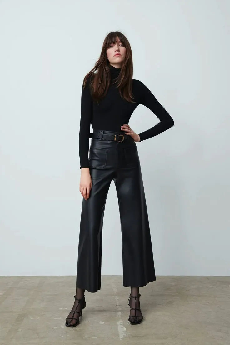 Woman wearing a black turtleneck and leather pants against a white background