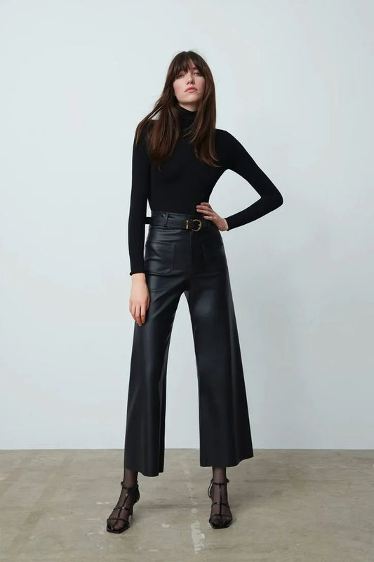 Woman wearing a black turtleneck and leather pants against a white background