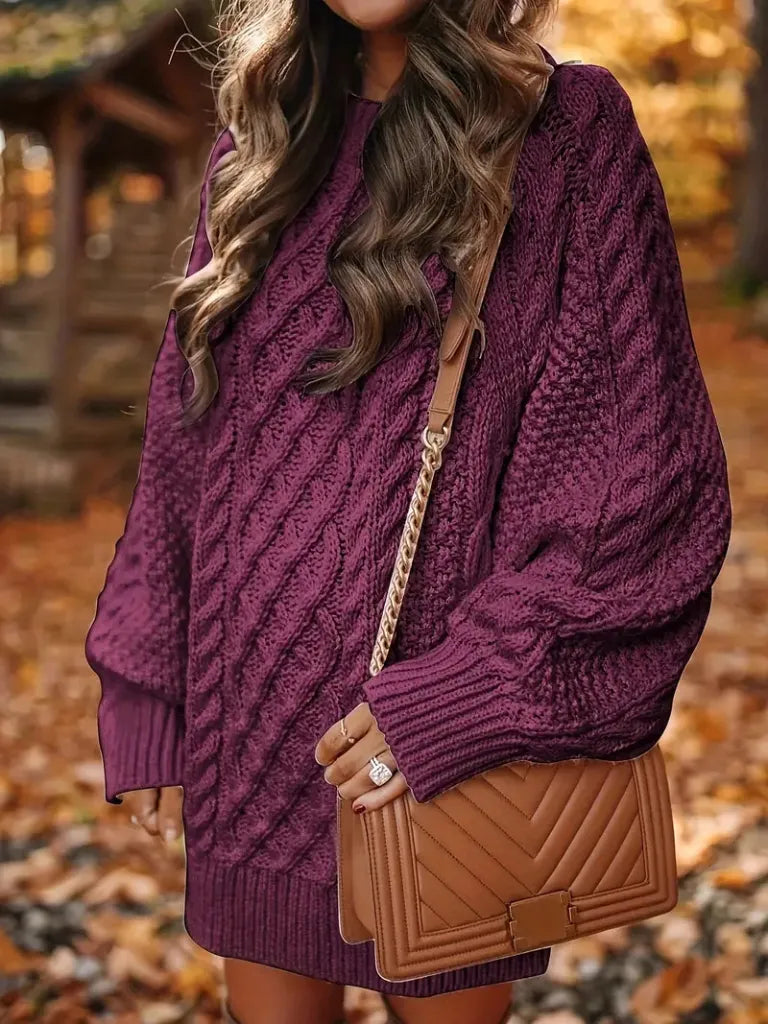Person wearing a purple cable knit sweater with a brown handbag in an autumn setting