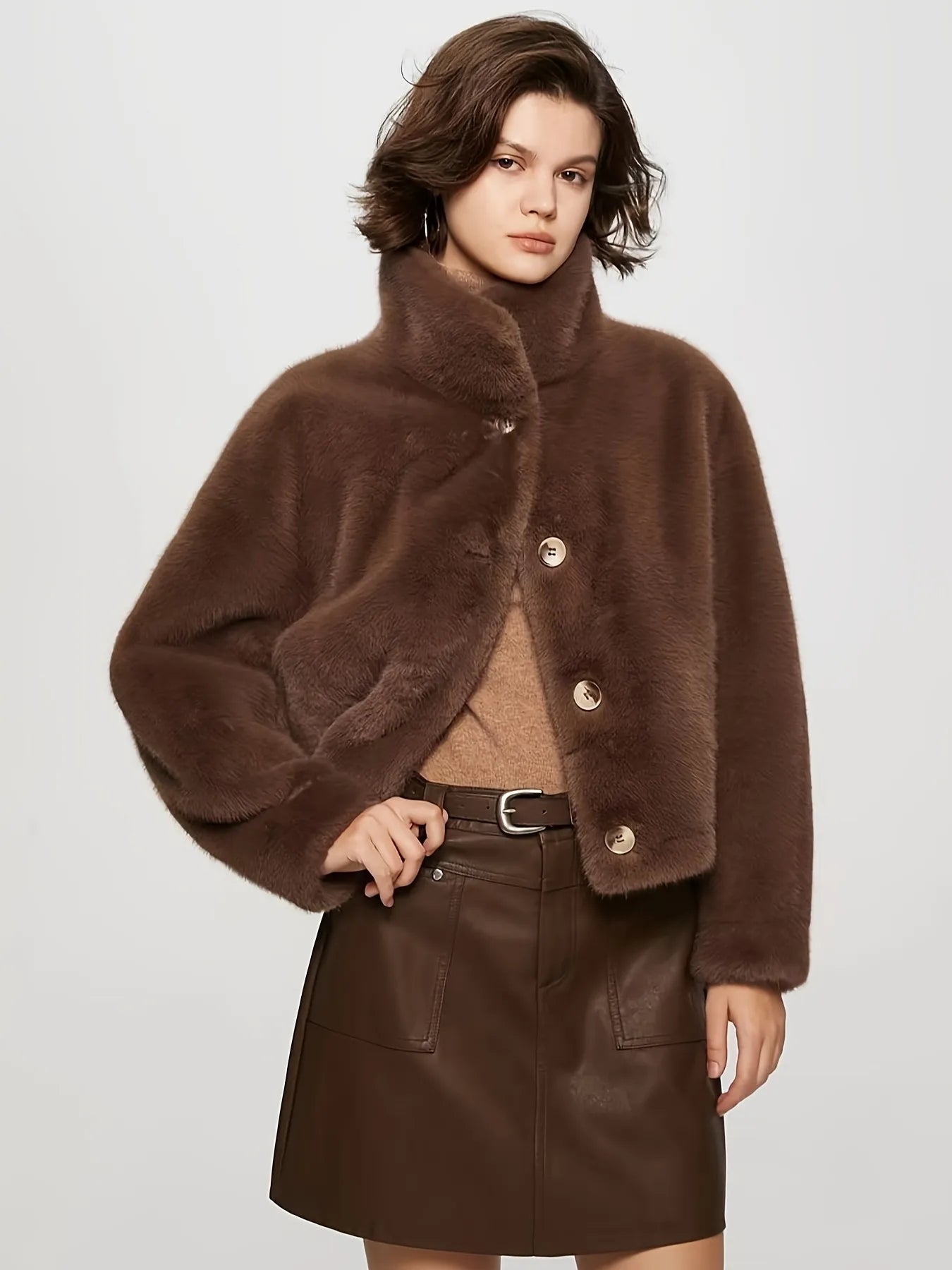 Woman wearing a brown coat with fur collar and leather skirt on a light gray background