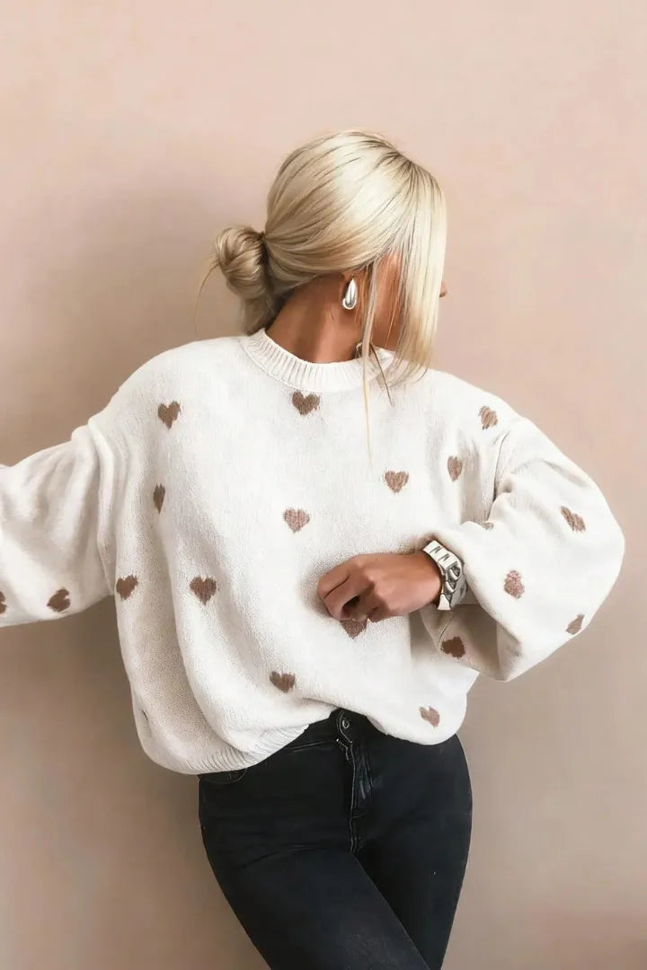 Person wearing a white sweater with heart patterns against a beige background