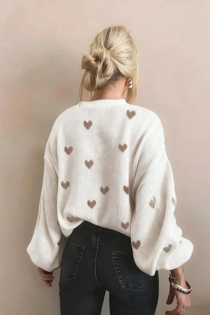 Person wearing a white sweater with heart patterns on a plain background
