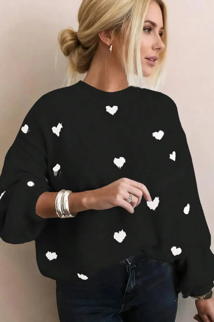 Woman wearing a black sweater with white heart patterns against a plain background