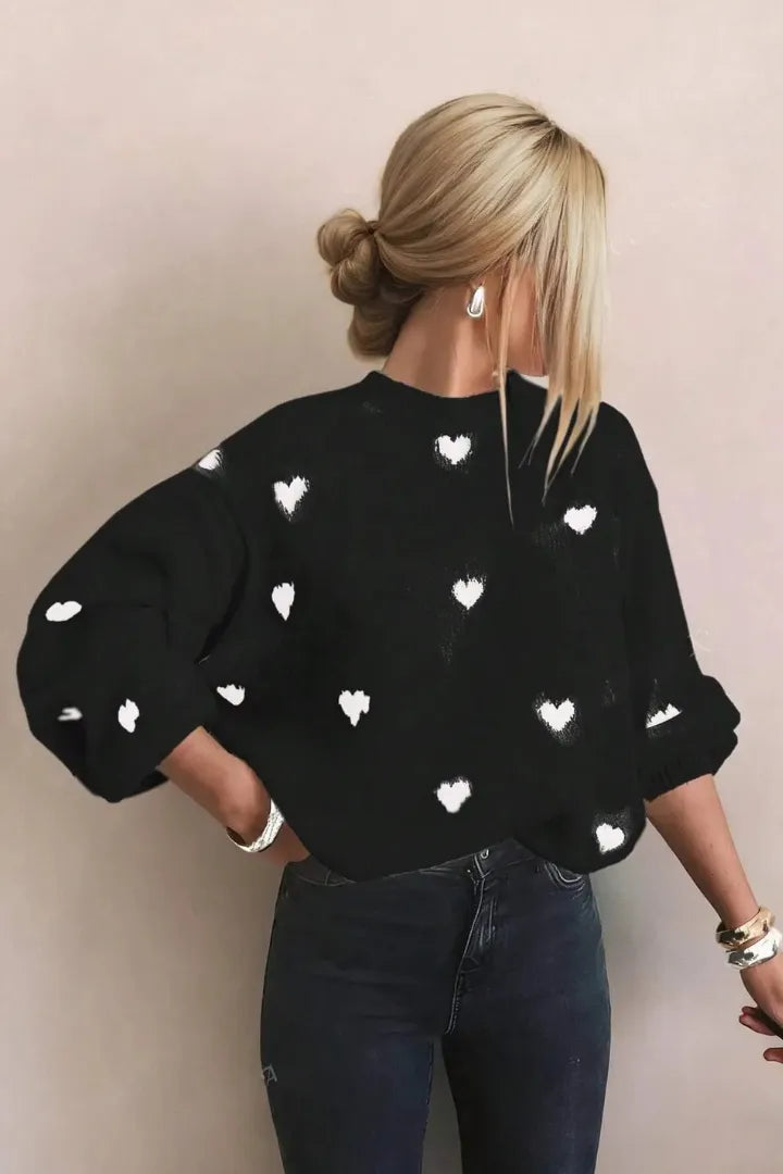 Person wearing a black sweater with white heart patterns against a beige background