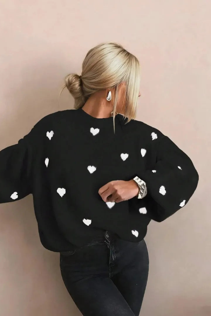 Person wearing a black sweater with white heart patterns against a beige background