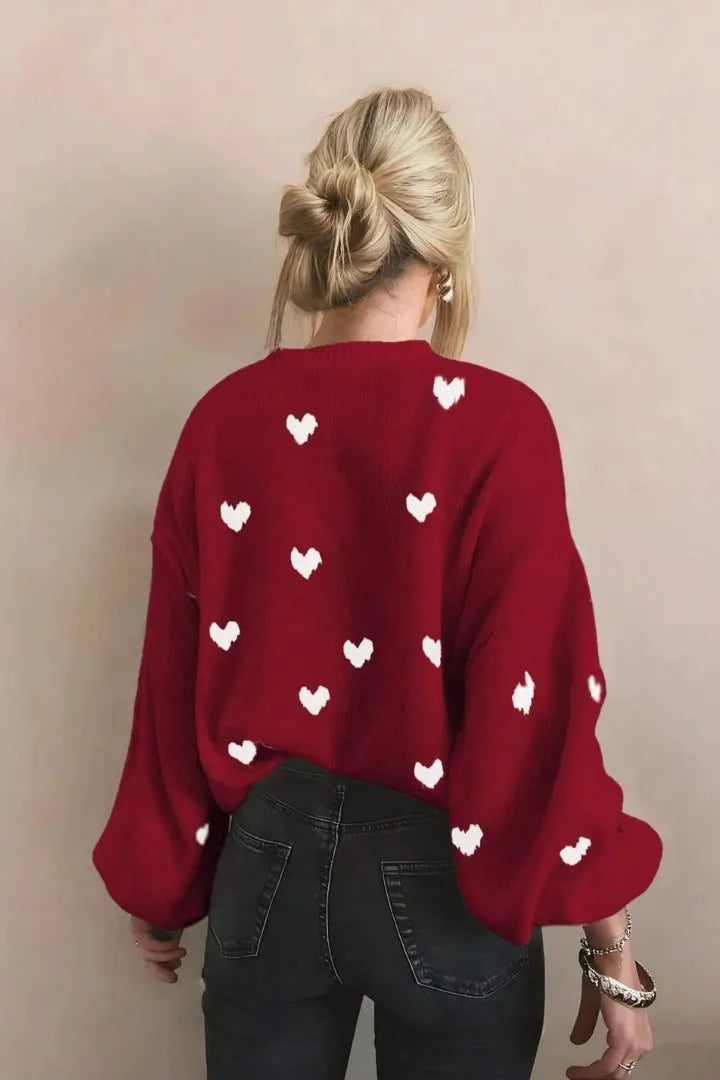 Red sweater with white heart patterns worn by a person against a beige background