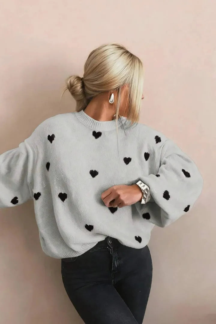 Person wearing a gray sweater with black heart patterns on a beige background