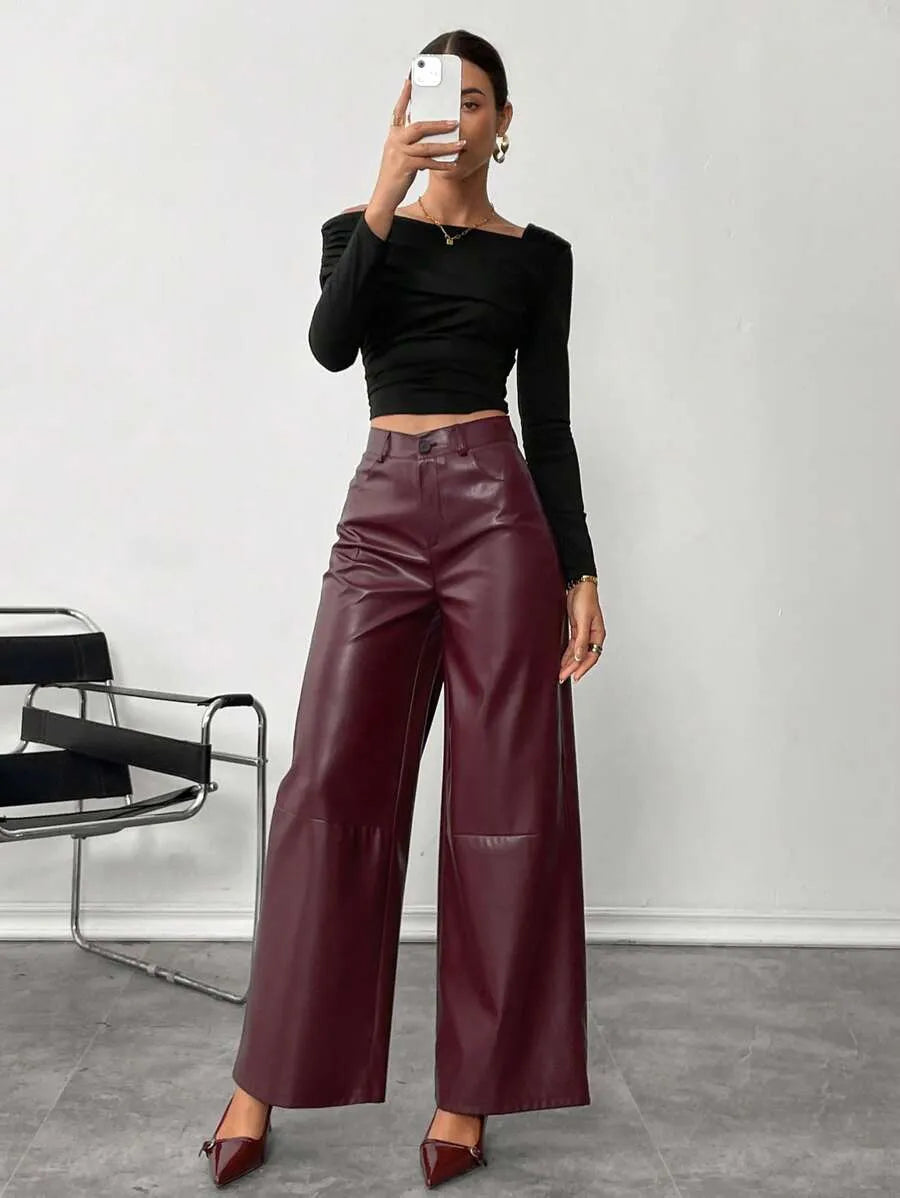 Person wearing maroon leather wide-leg pants with a black top and shoes in a minimalistic setting.