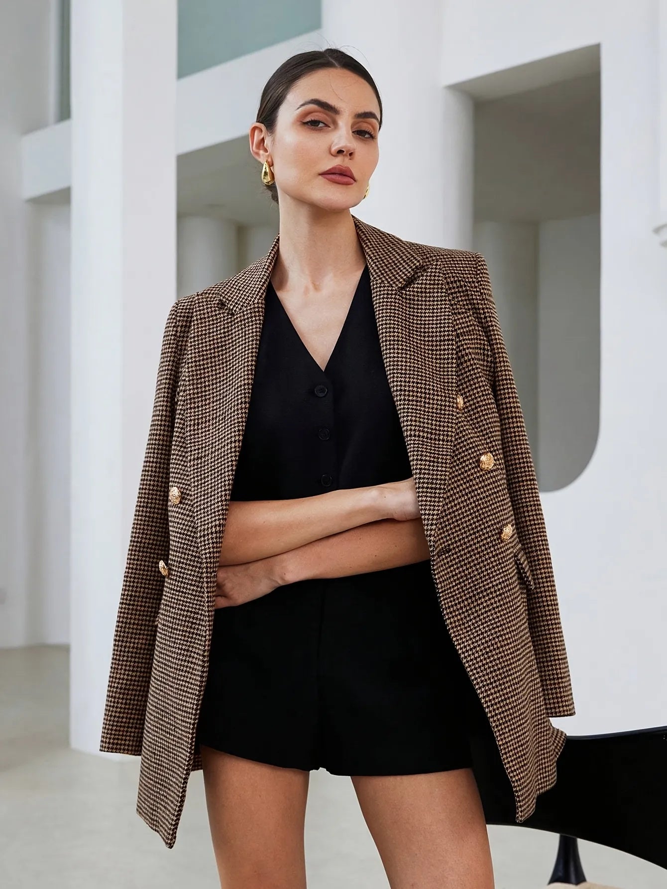 Woman wearing a brown blazer over a black top and shorts in a minimalistic setting