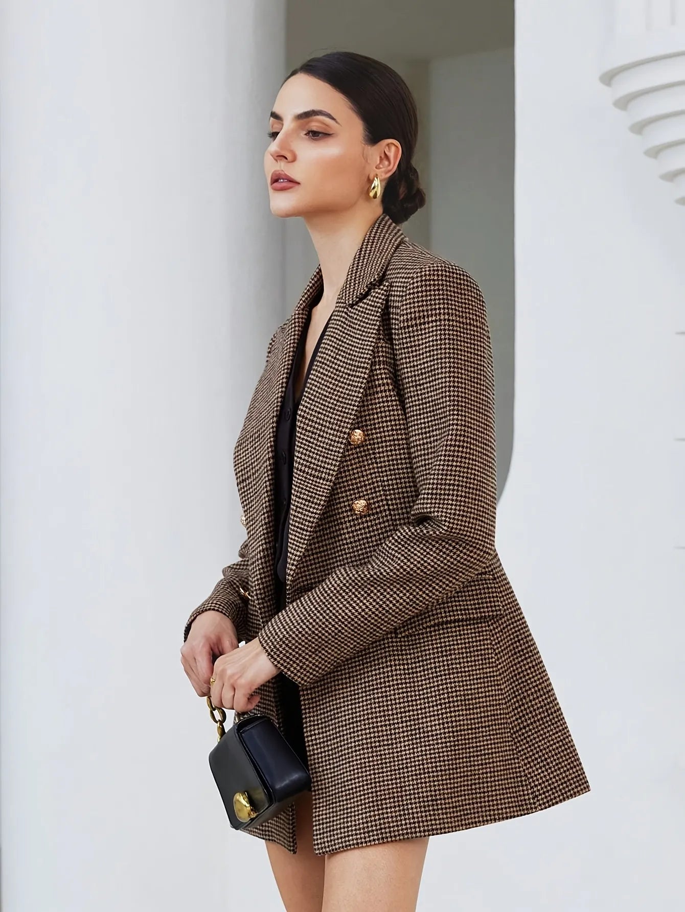 Woman wearing a brown checkered blazer over a black dress, holding a black handbag.