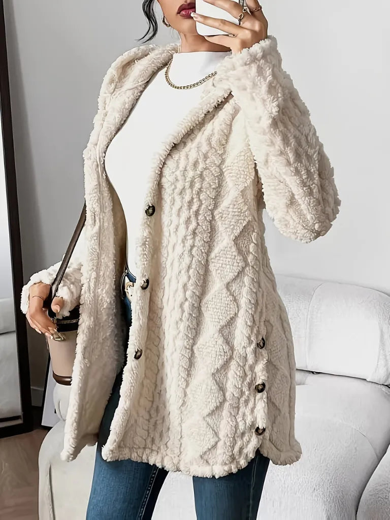 Person wearing a beige cable knit cardigan with buttons indoors.