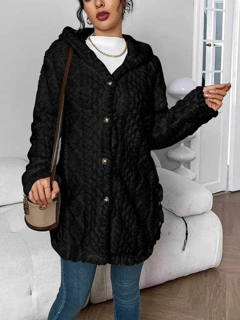 Woman wearing a black textured coat in a room with white furniture.