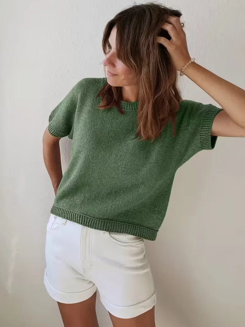 Person wearing a green knitted sweater and white shorts against a plain background