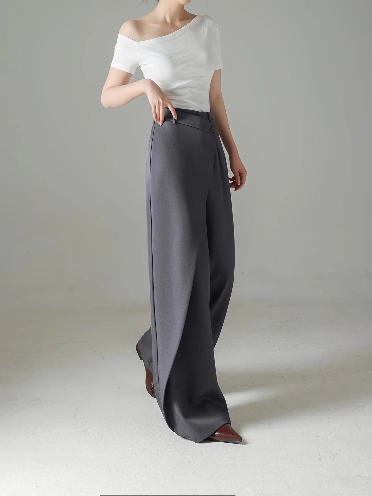 Person wearing a white off-shoulder top and gray wide-leg pants on a plain background