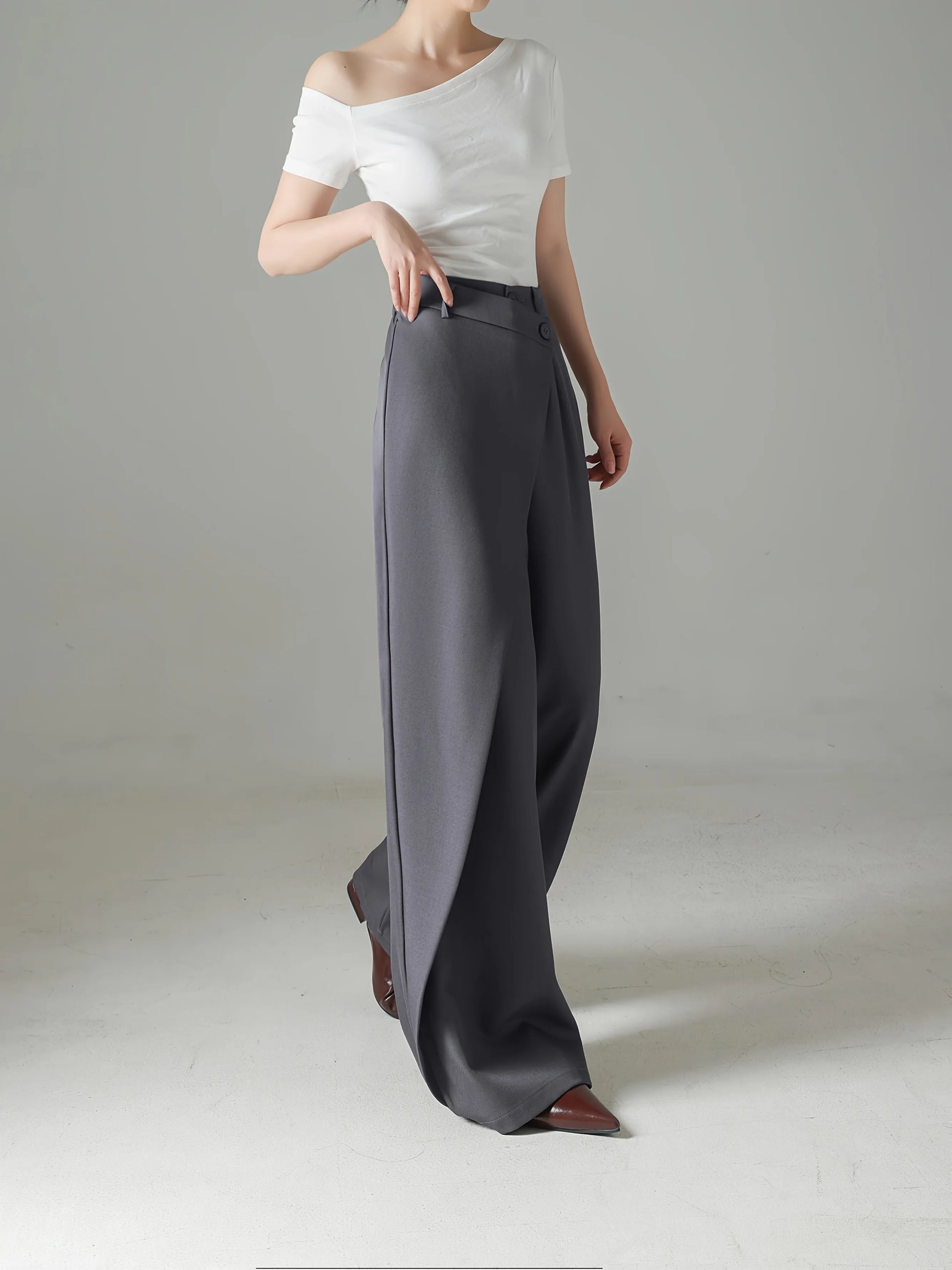 Person wearing a white off-shoulder top and gray wide-leg pants on a plain background