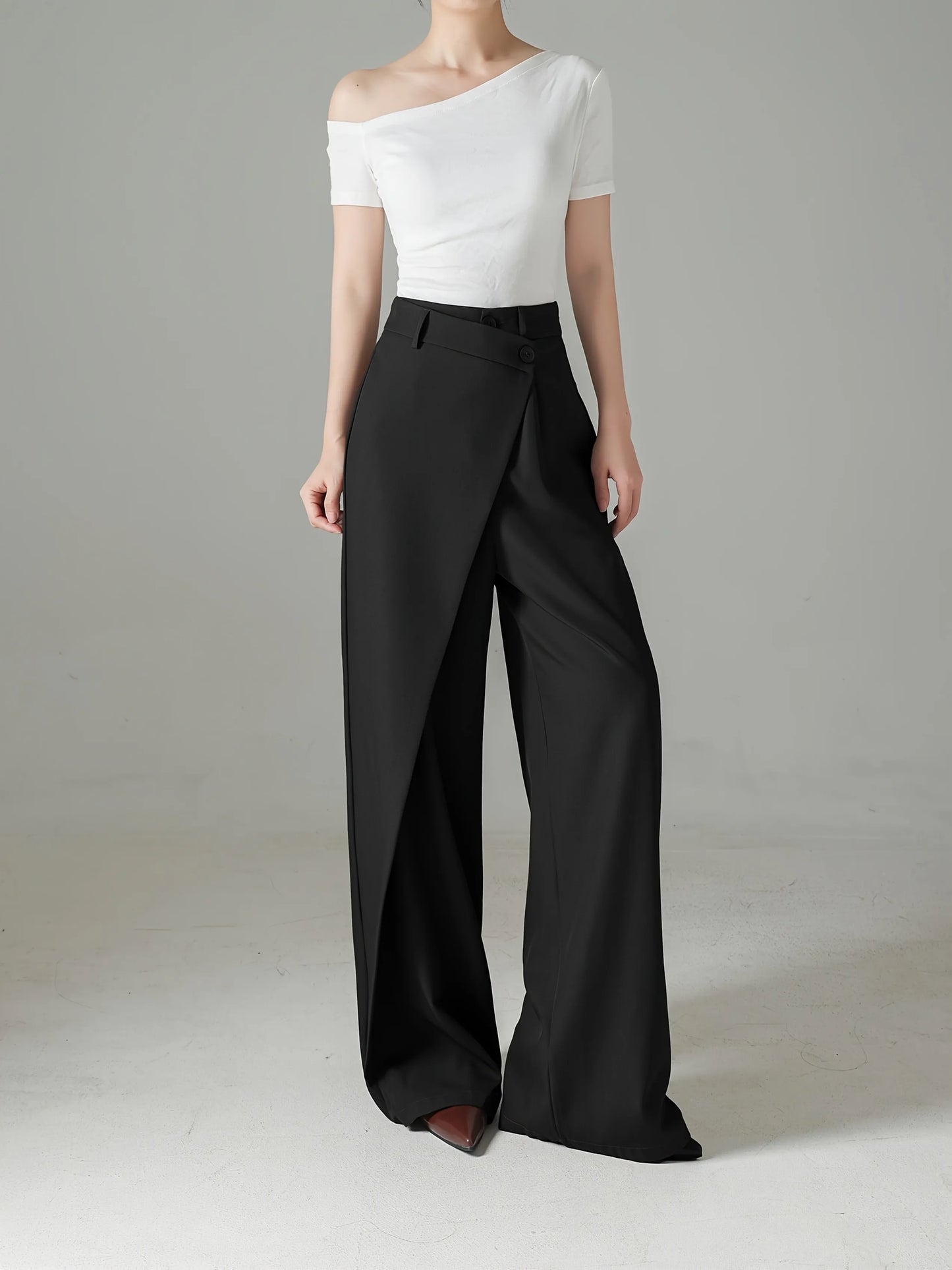 Person wearing a white off-shoulder top and black wide-leg pants on a plain background
