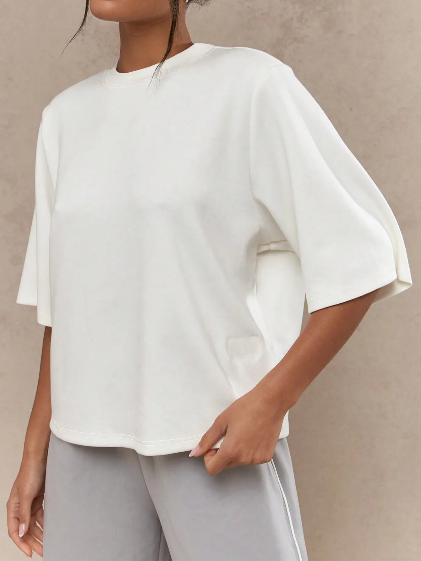 Person wearing a white oversized t-shirt and light gray pants against a beige background