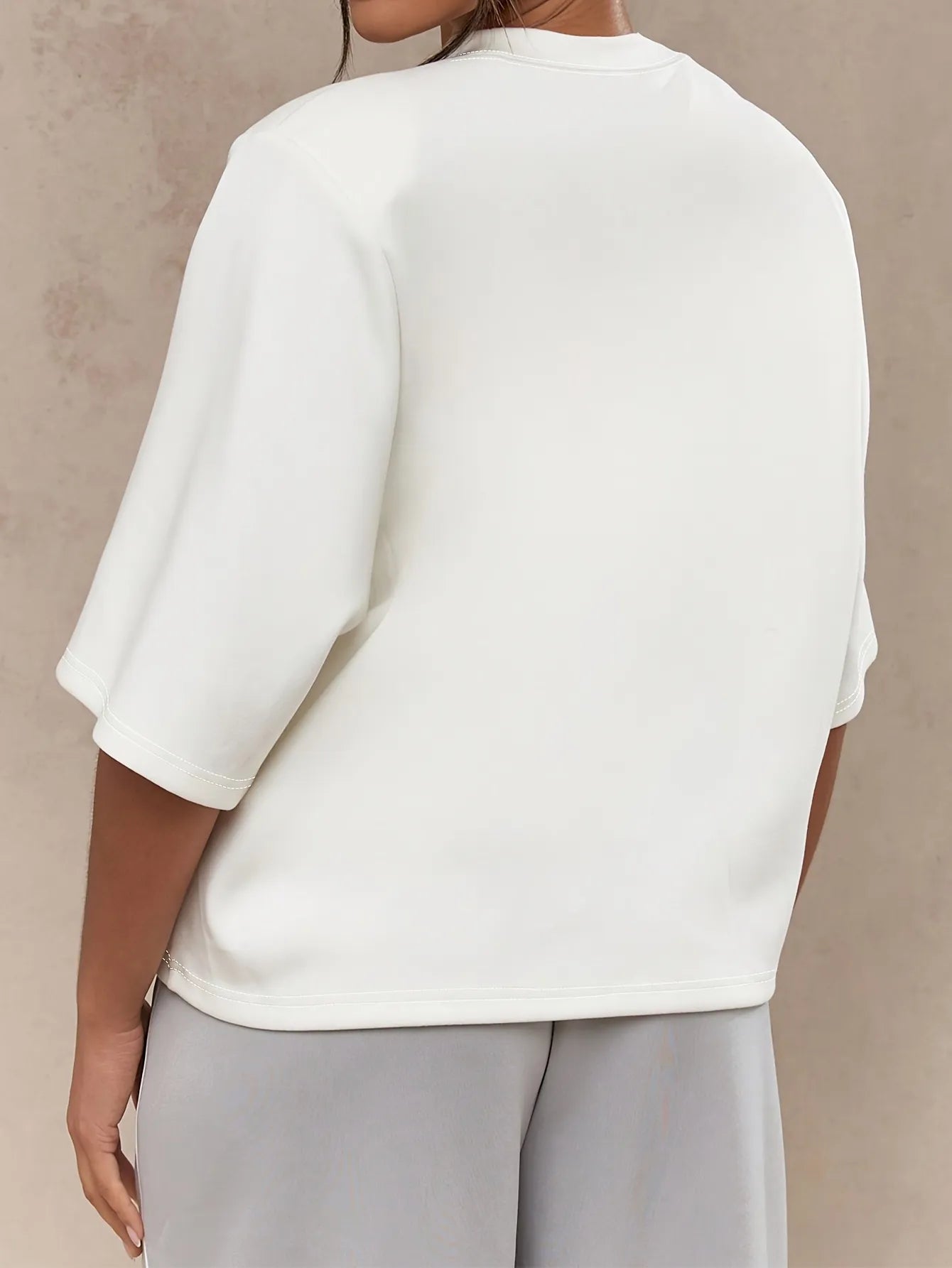 Person wearing a white blouse and light gray pants against a beige background