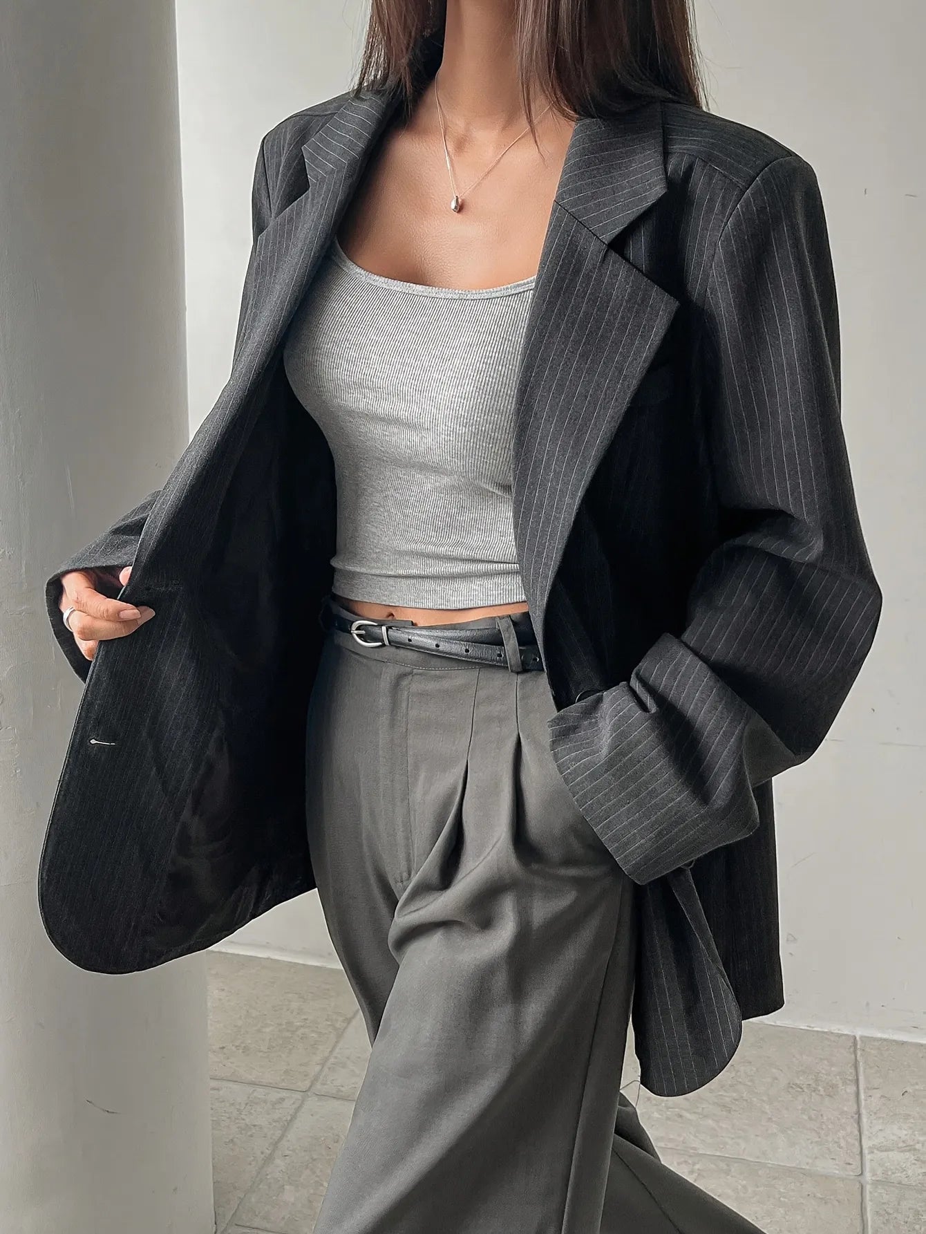 Person wearing a dark pinstripe blazer over a gray top and pants on a neutral background