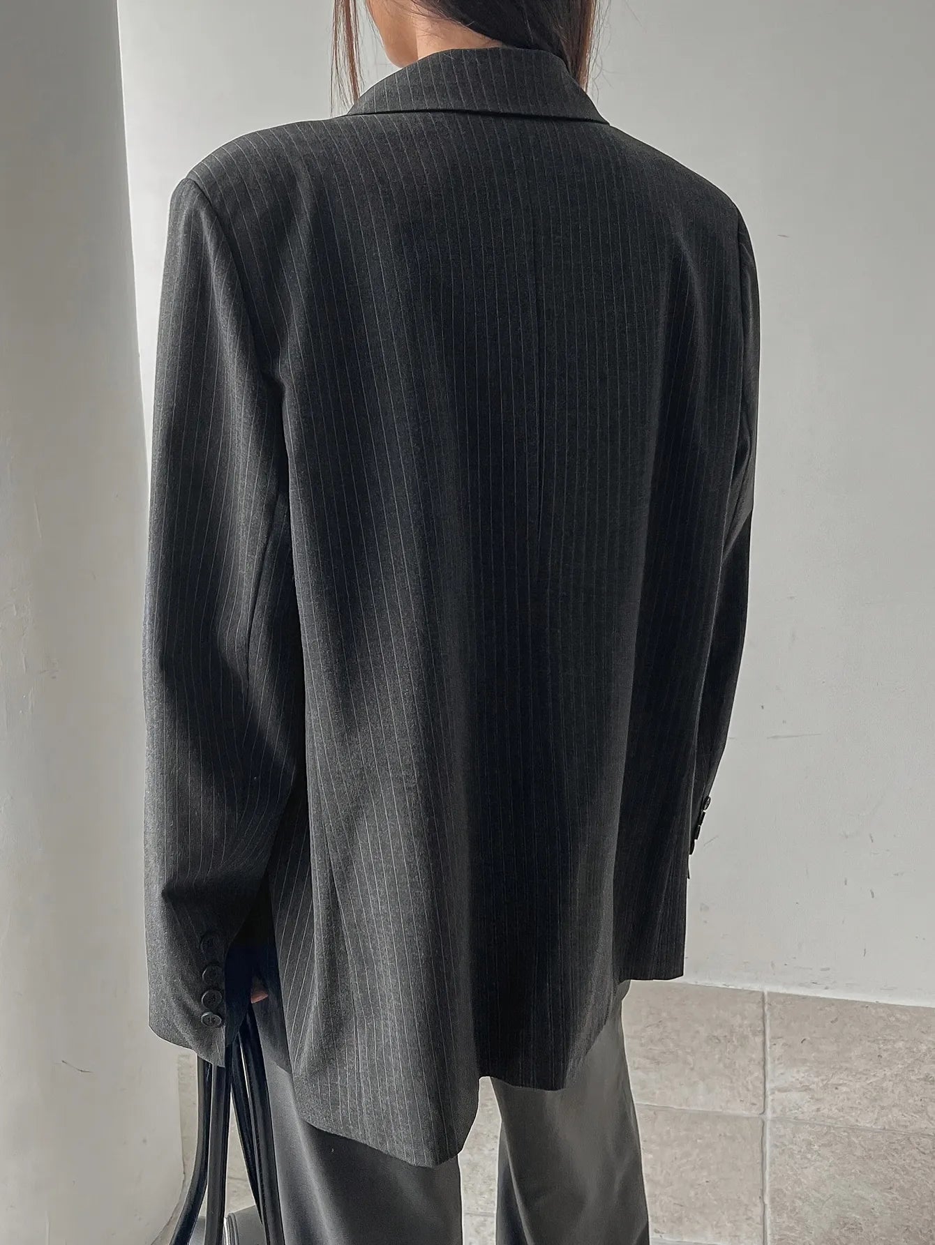 Person wearing a dark pinstripe blazer over a gray top and pants on a neutral background