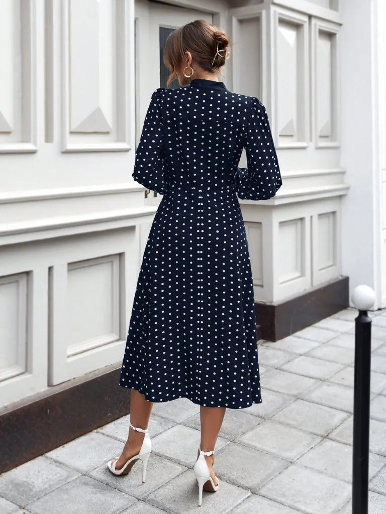 Woman wearing a navy blue dress with white polka dots in an urban setting.