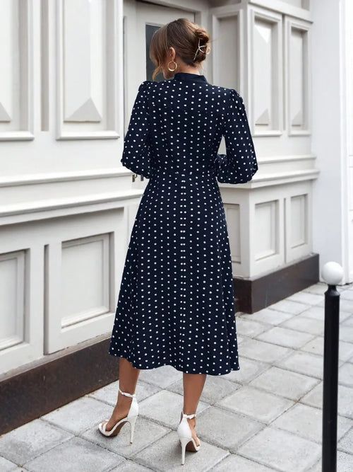 Woman wearing a navy blue dress with white polka dots in an urban setting.