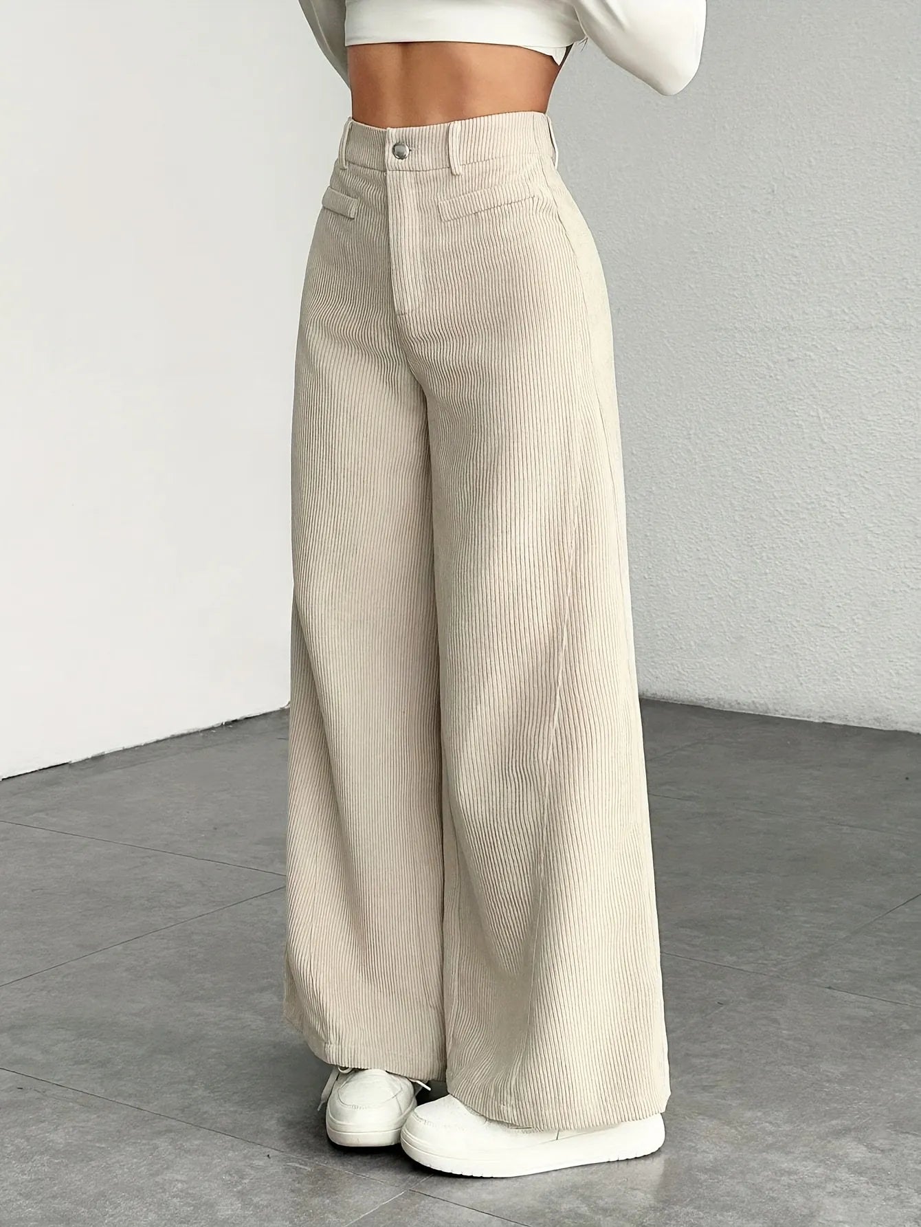 Beige wide-leg pants worn by a person on a gray floor with a neutral background