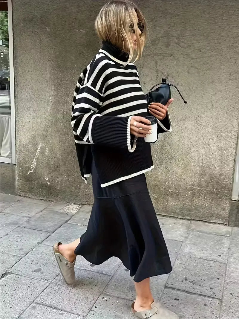 Person wearing a black and white striped sweater and dark skirt walking on a sidewalk.