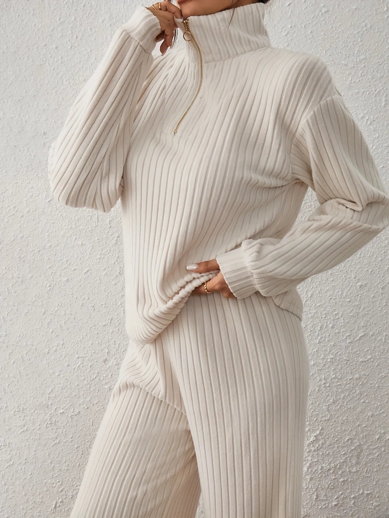 Person wearing a cream ribbed knit sweater and pants against a light gray background