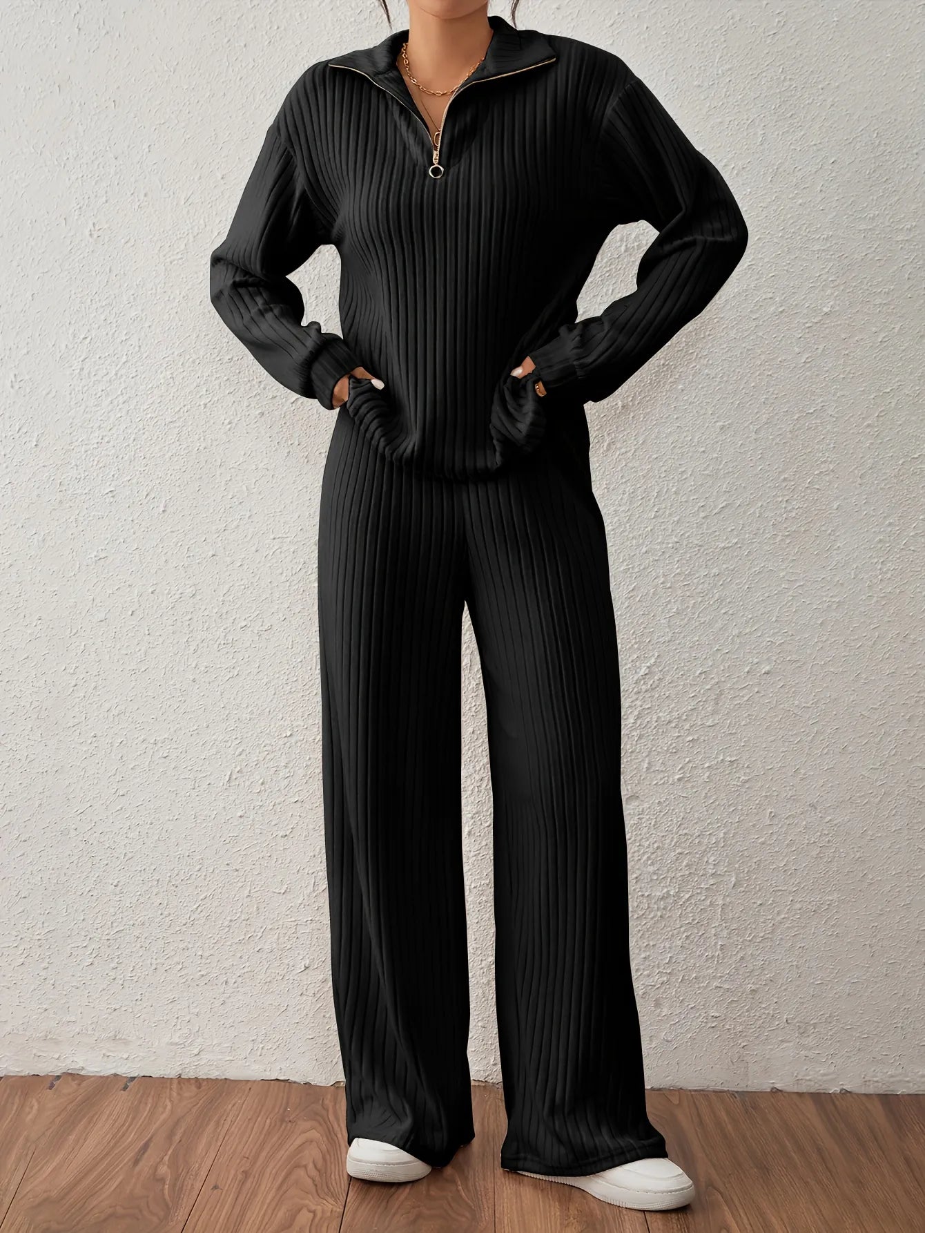 Person wearing a black ribbed knit outfit with wide-leg pants against a white wall.