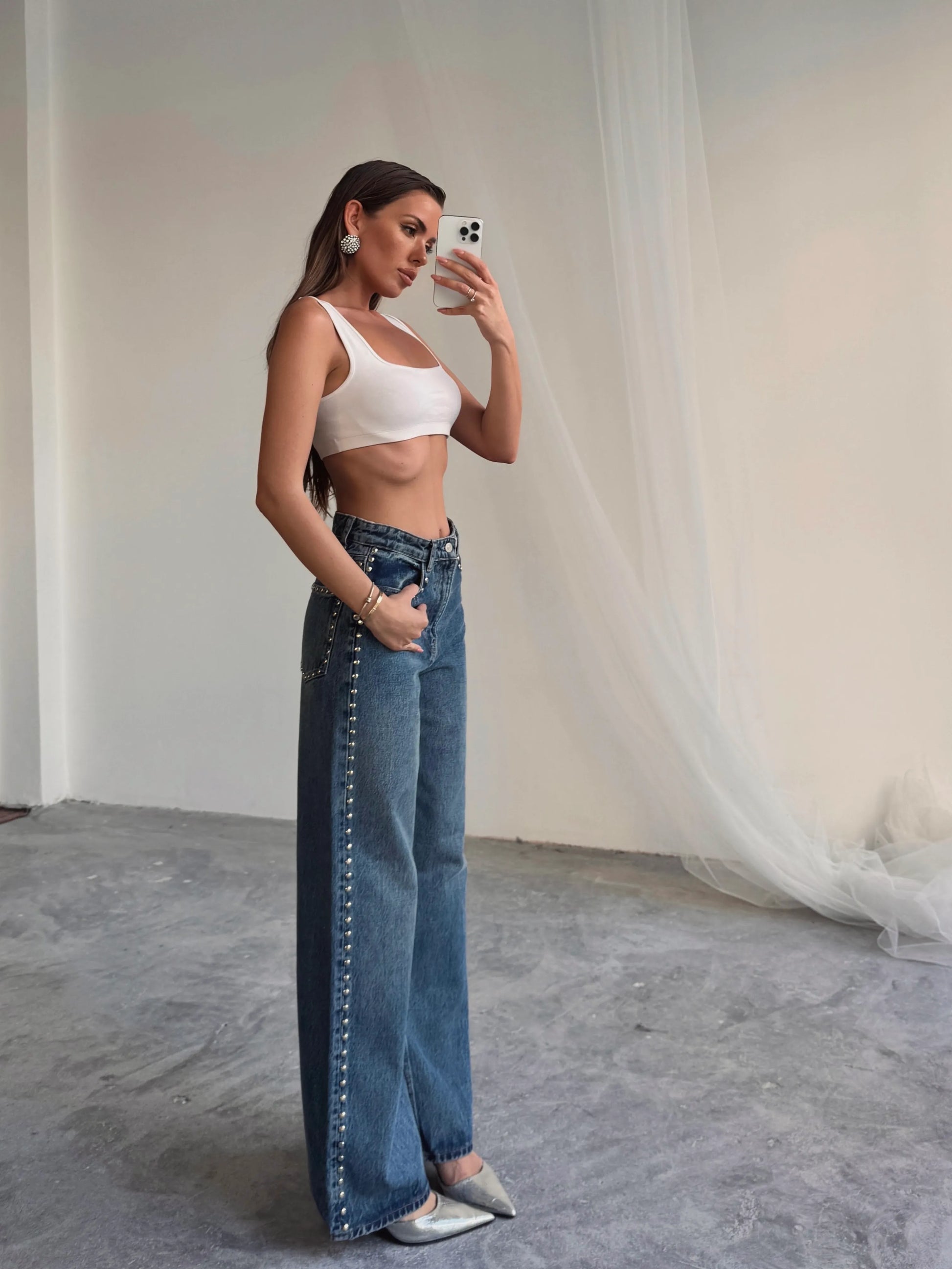 Woman taking a mirror selfie wearing a white top and blue jeans.