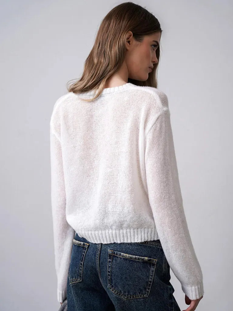 Woman wearing a white sweater and blue jeans against a plain background