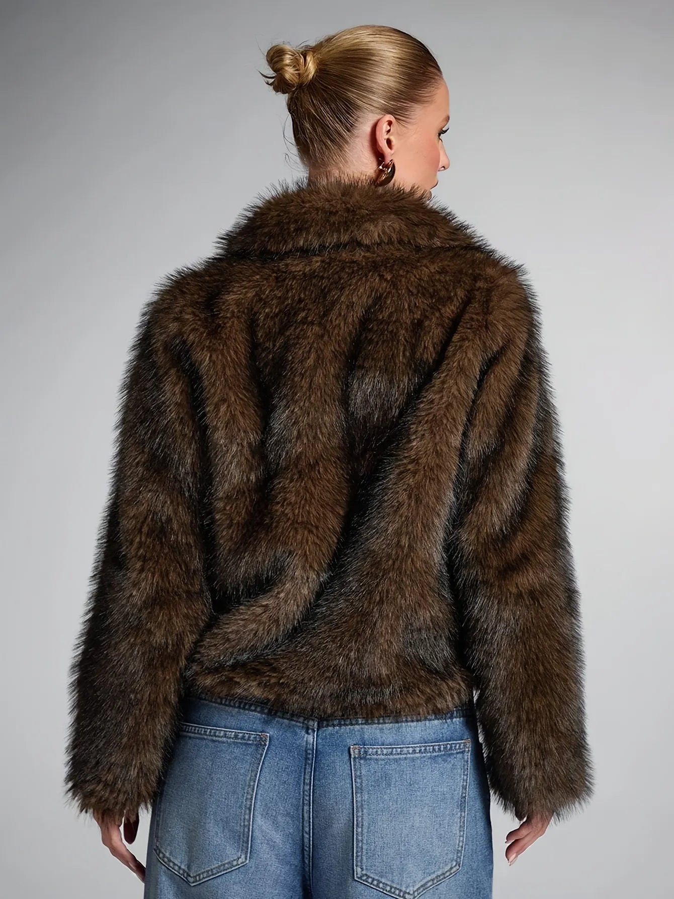 Person wearing a brown fur coat and blue jeans on a gray background