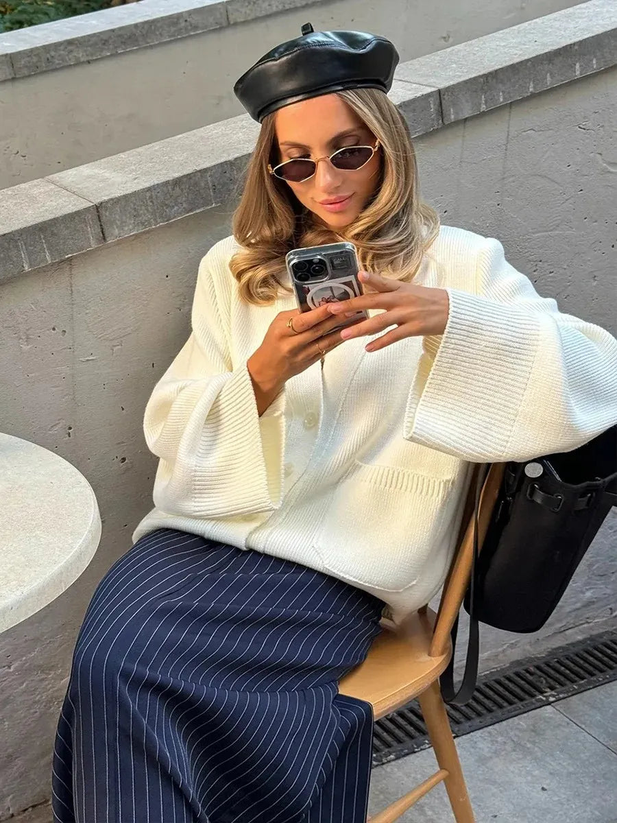 Woman in a white sweater and black beret taking a selfie outdoors.