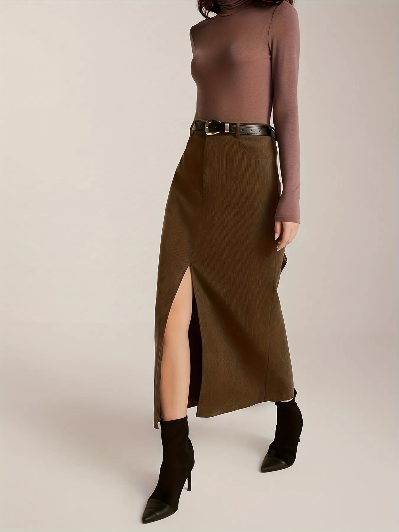 Person wearing a brown long-sleeve top and olive green skirt with a belt, standing against a plain background.