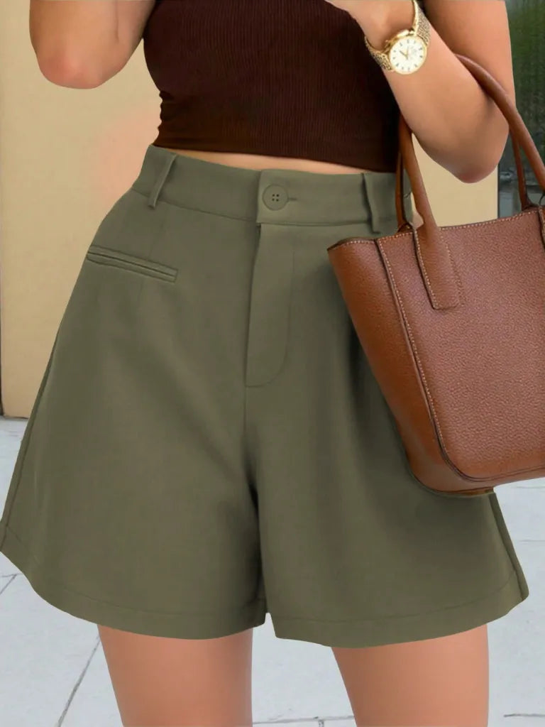 Person wearing green shorts and a brown top, holding a brown handbag.