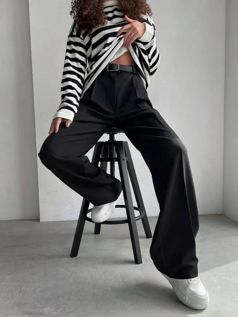 Person wearing a black and white striped sweater and black pants sitting on a stool.