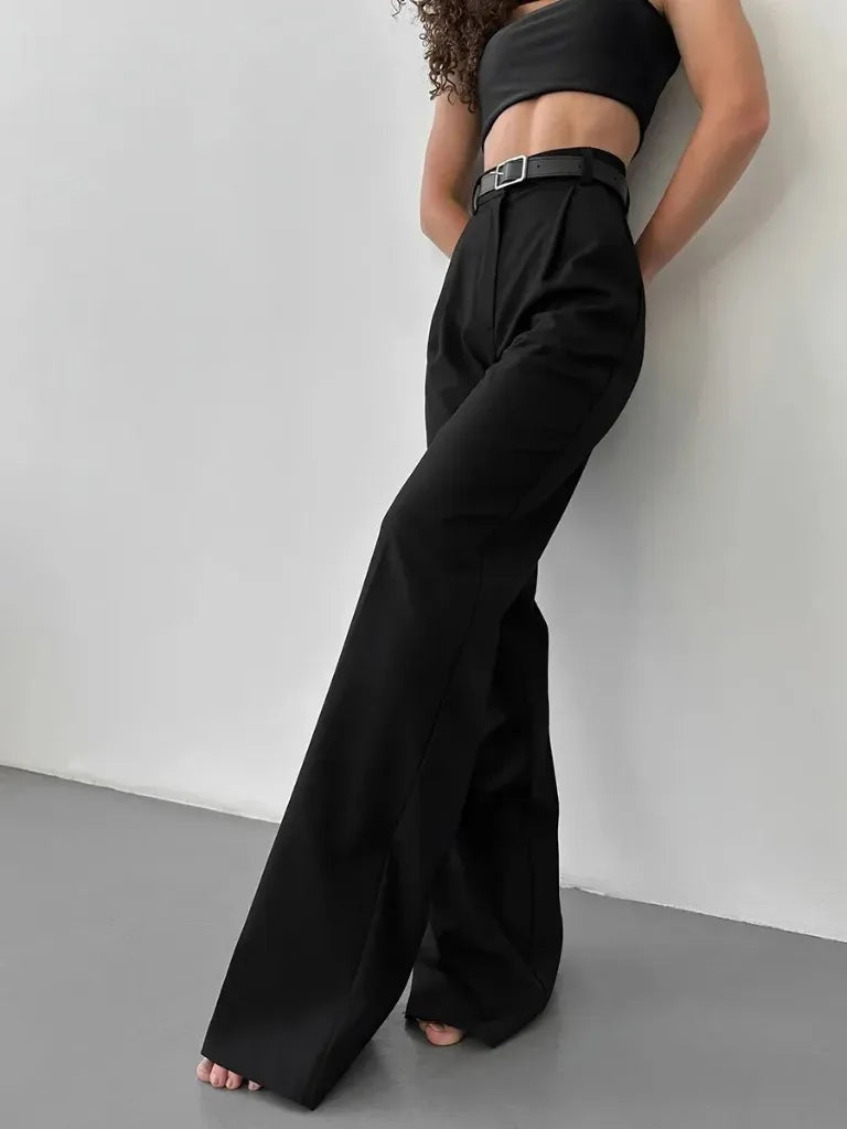 Person wearing a black outfit with wide-leg pants against a white wall.