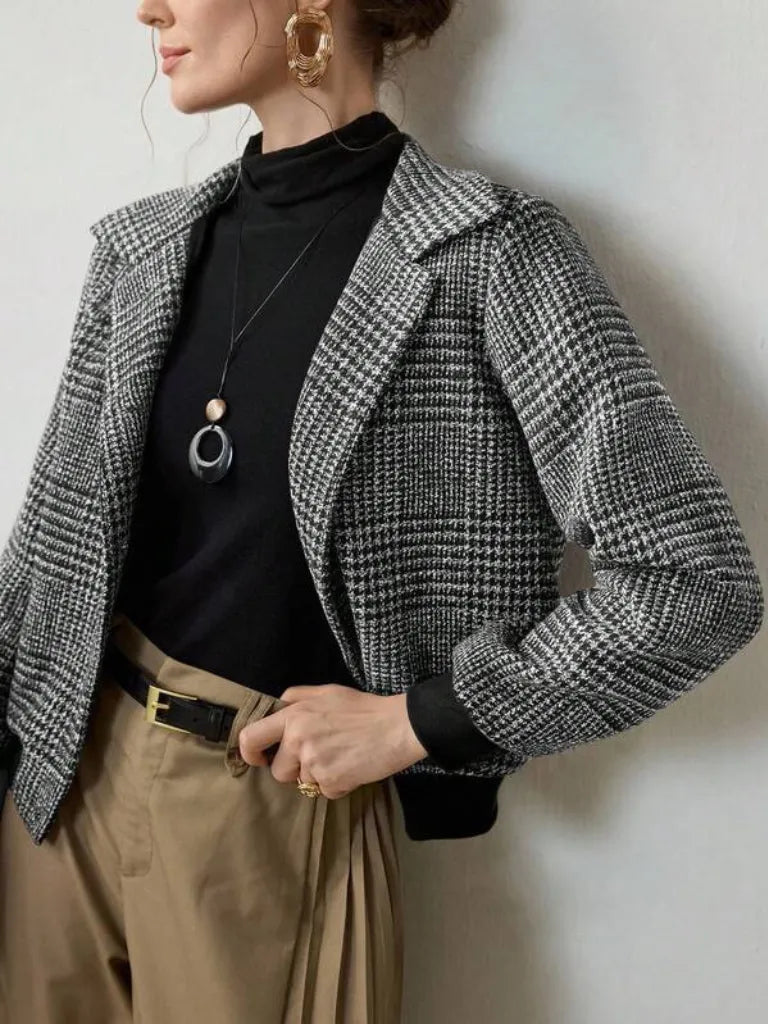 Person wearing a checkered blazer over a black top with beige pants against a neutral background