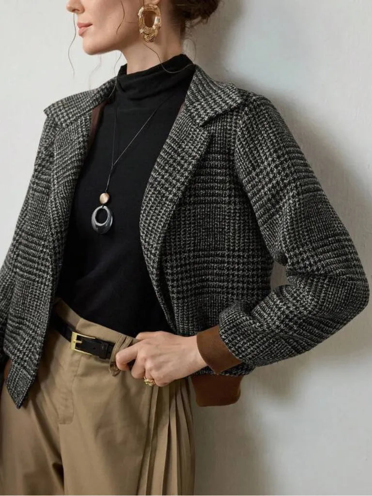 Person wearing a gray checkered blazer over a black top with beige pants against a neutral background