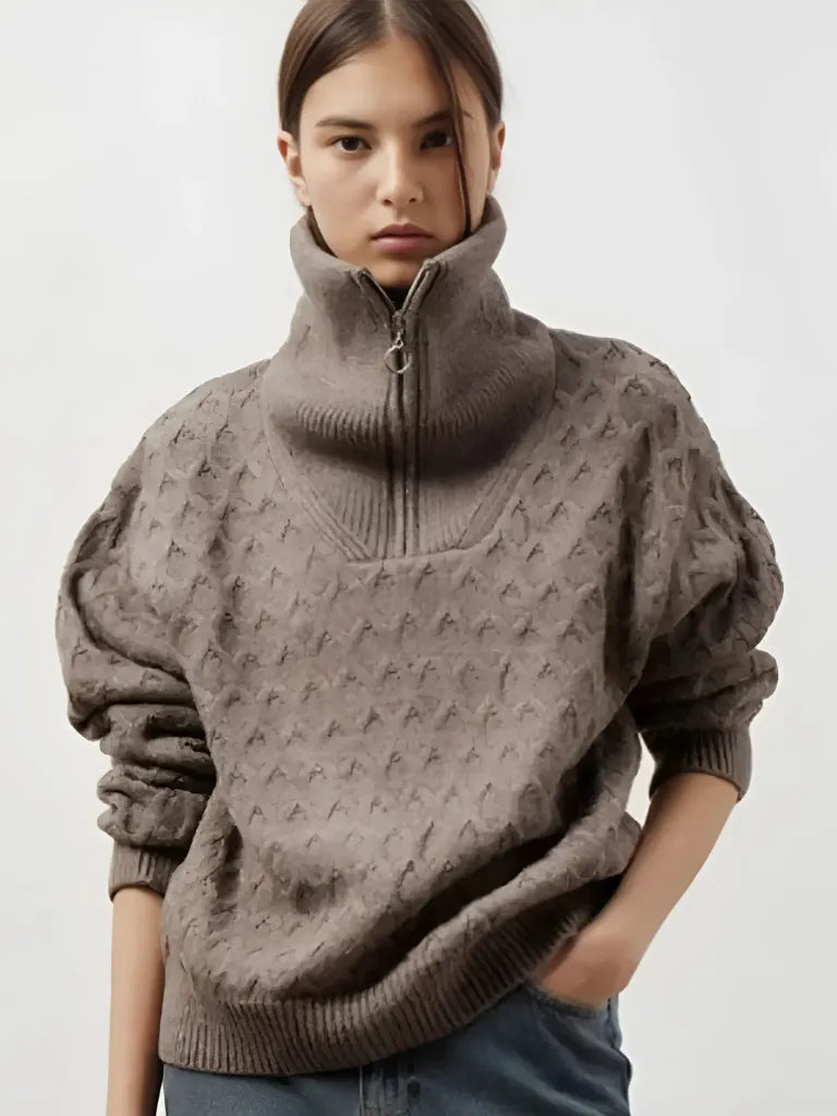 Person wearing a brown patterned sweater with a high collar on a plain background