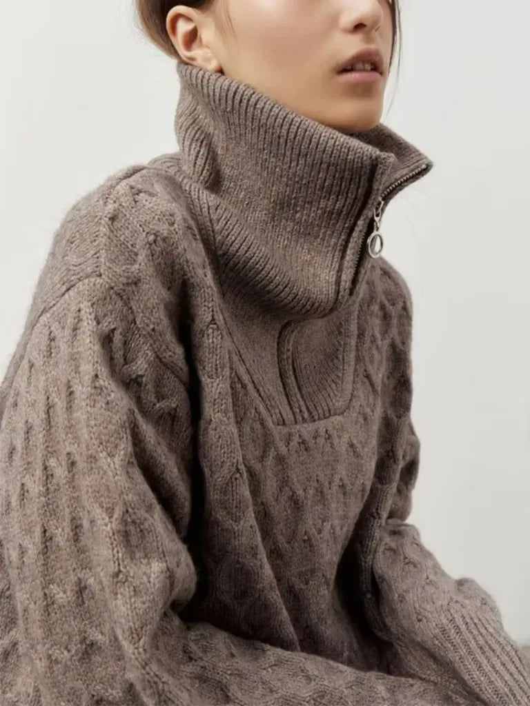 Person wearing a brown cable knit sweater with a high collar on a plain background