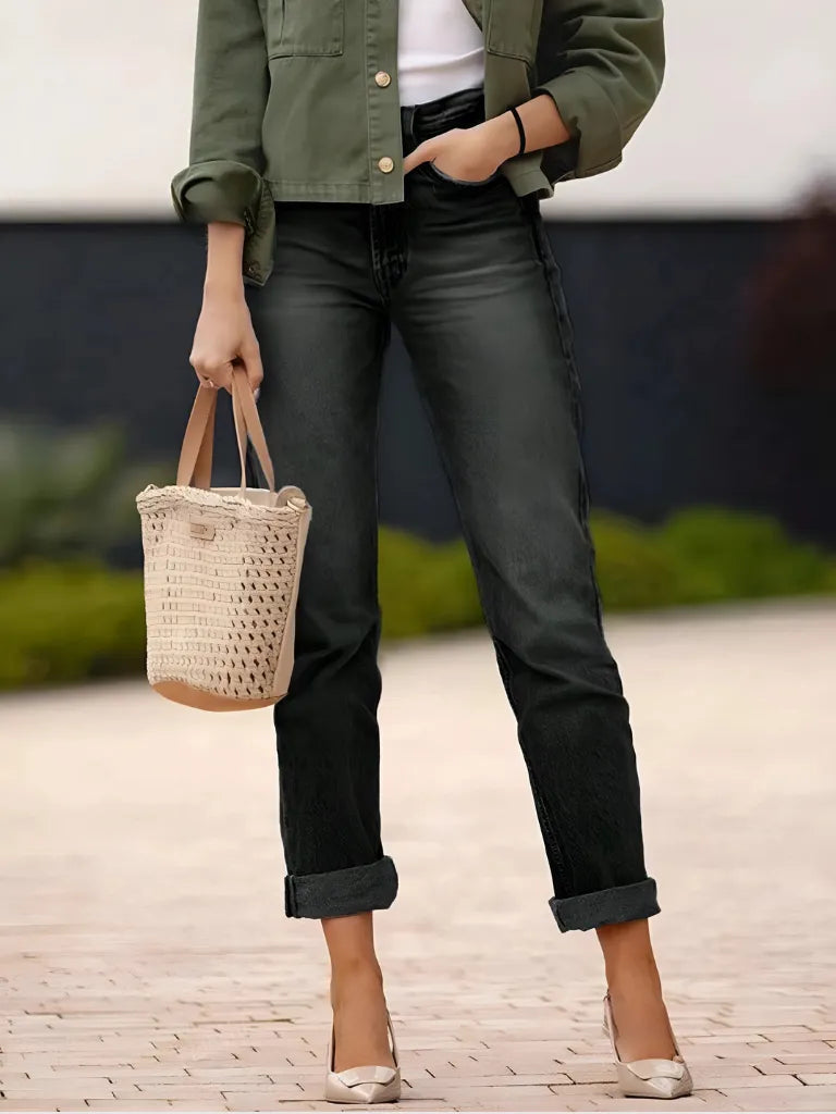 Person wearing a green jacket and black jeans, holding a woven bag on a blurred outdoor background