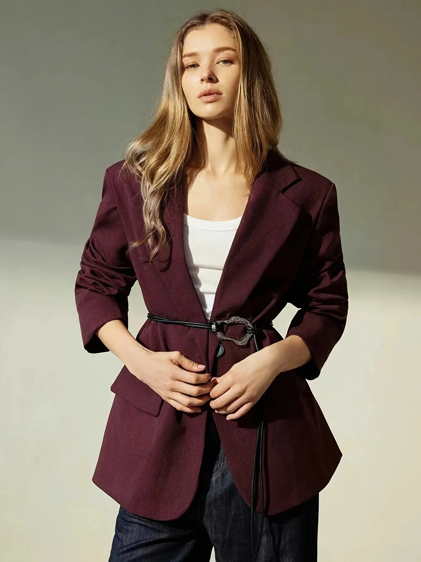 Woman wearing a burgundy blazer over a white top and dark pants on a neutral background