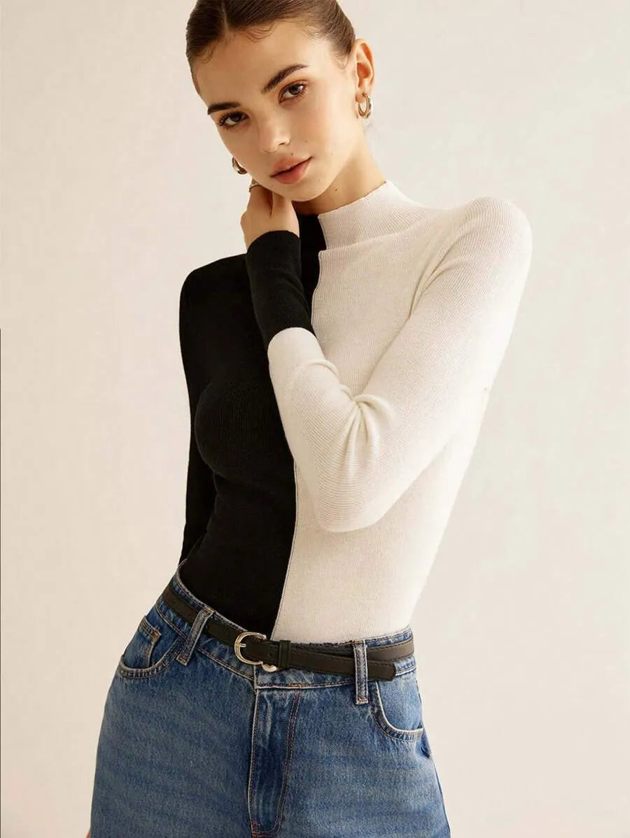 Woman wearing a black and white long-sleeve top with blue jeans on a light background