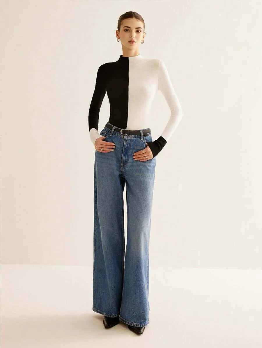 Person wearing a black and white top with blue jeans on a plain background